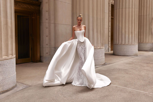 Model wearing a stunning shantung satin corset dress with a flowing train in an elegant architectural setting.