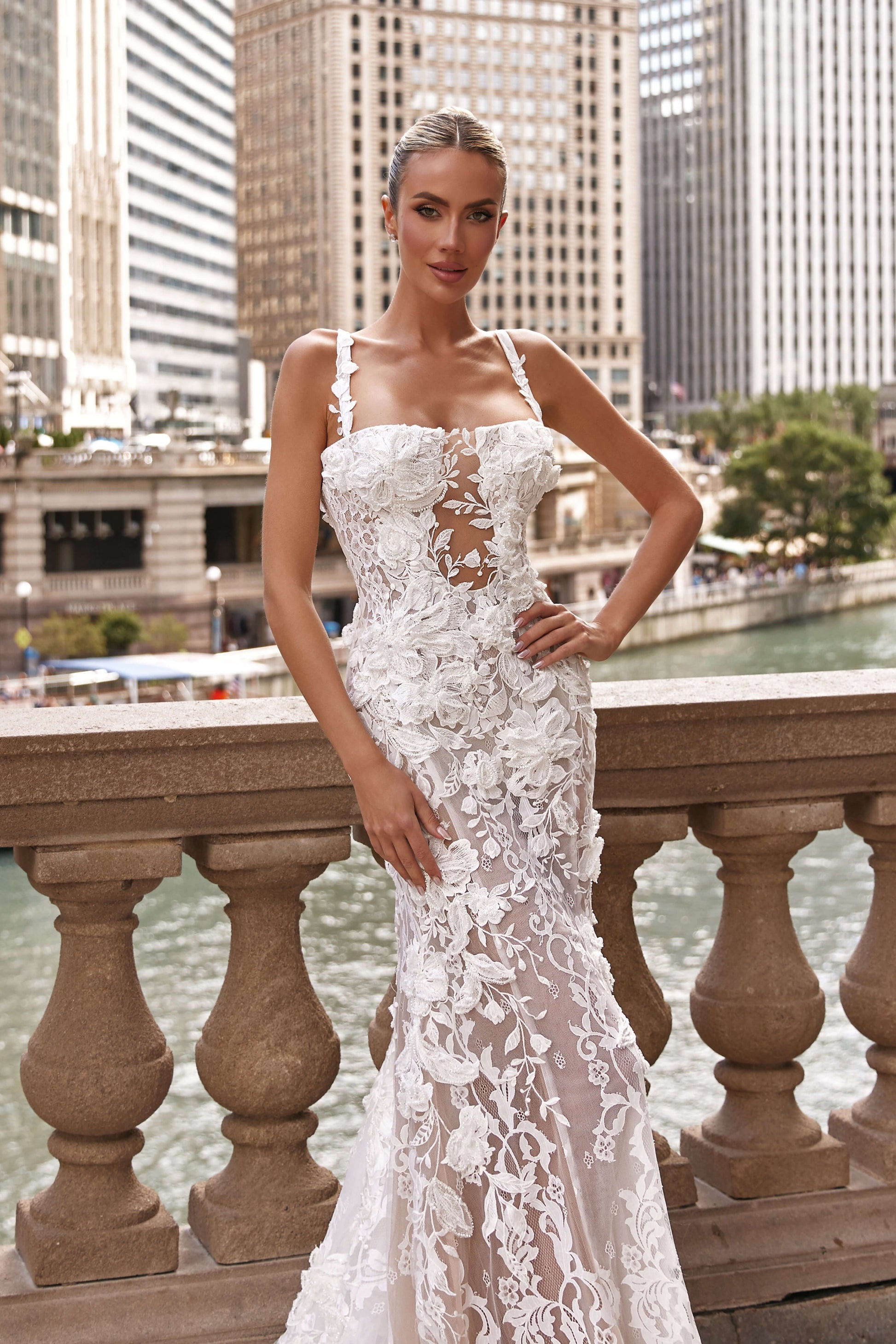 Model wearing a Chloe lined dress with intricate floral details by a river in a city setting.