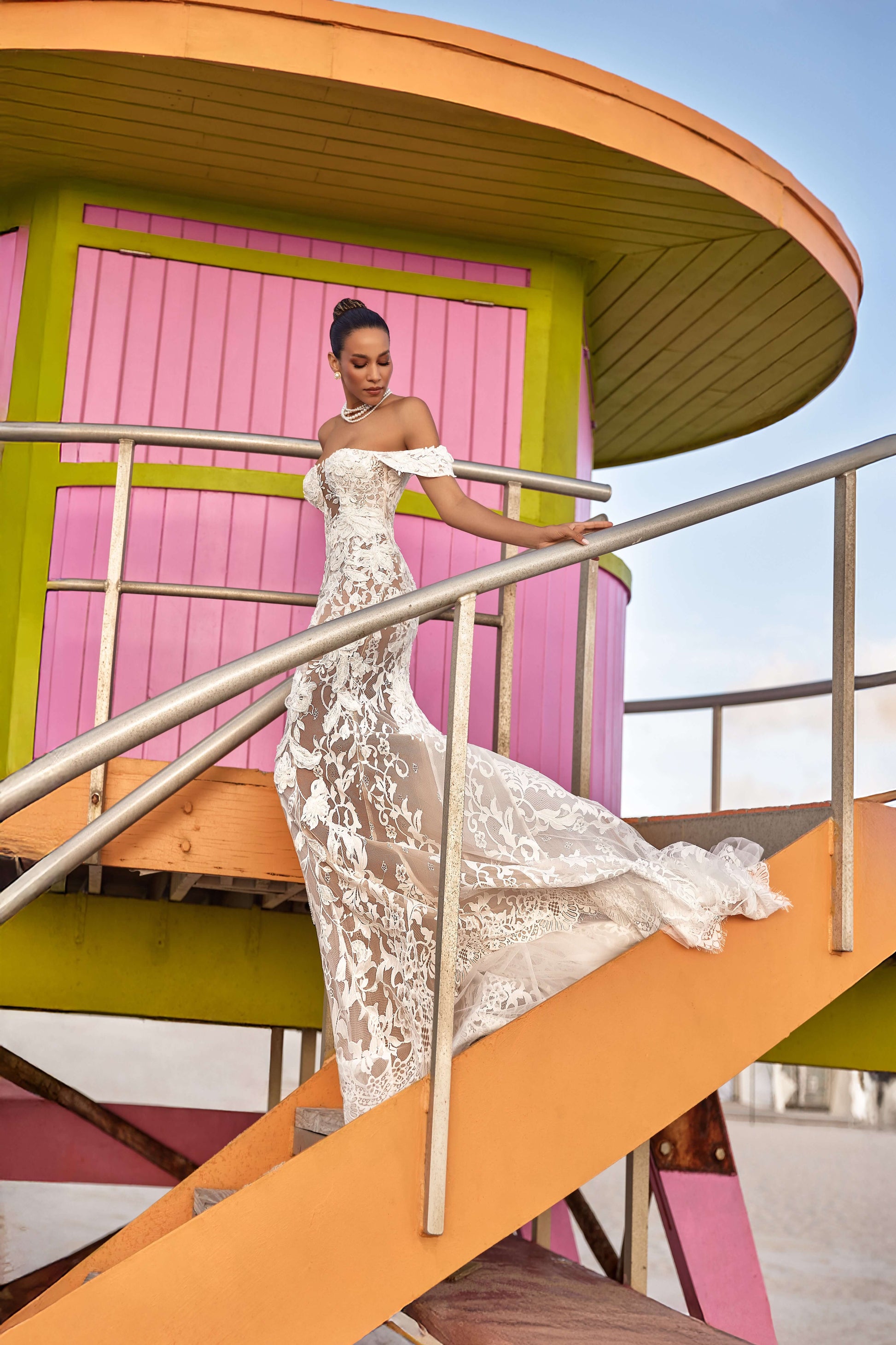 Model wearing Chloe lined dress on colorful beach lifeguard tower, showcasing off-the-shoulder silhouette and romantic detail.