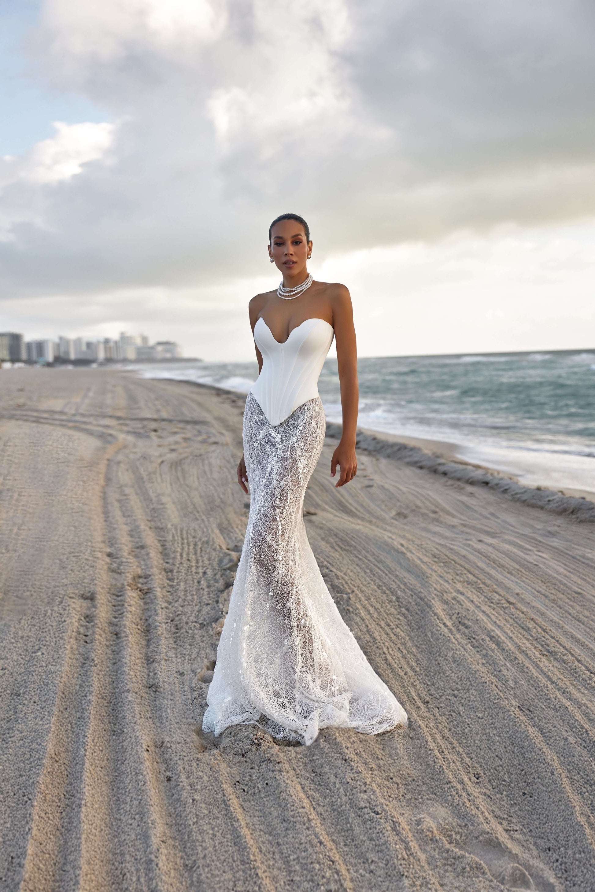 Modern corset skirt set showcased by a model on the beach, featuring a fitted bodice and flowing lace skirt.