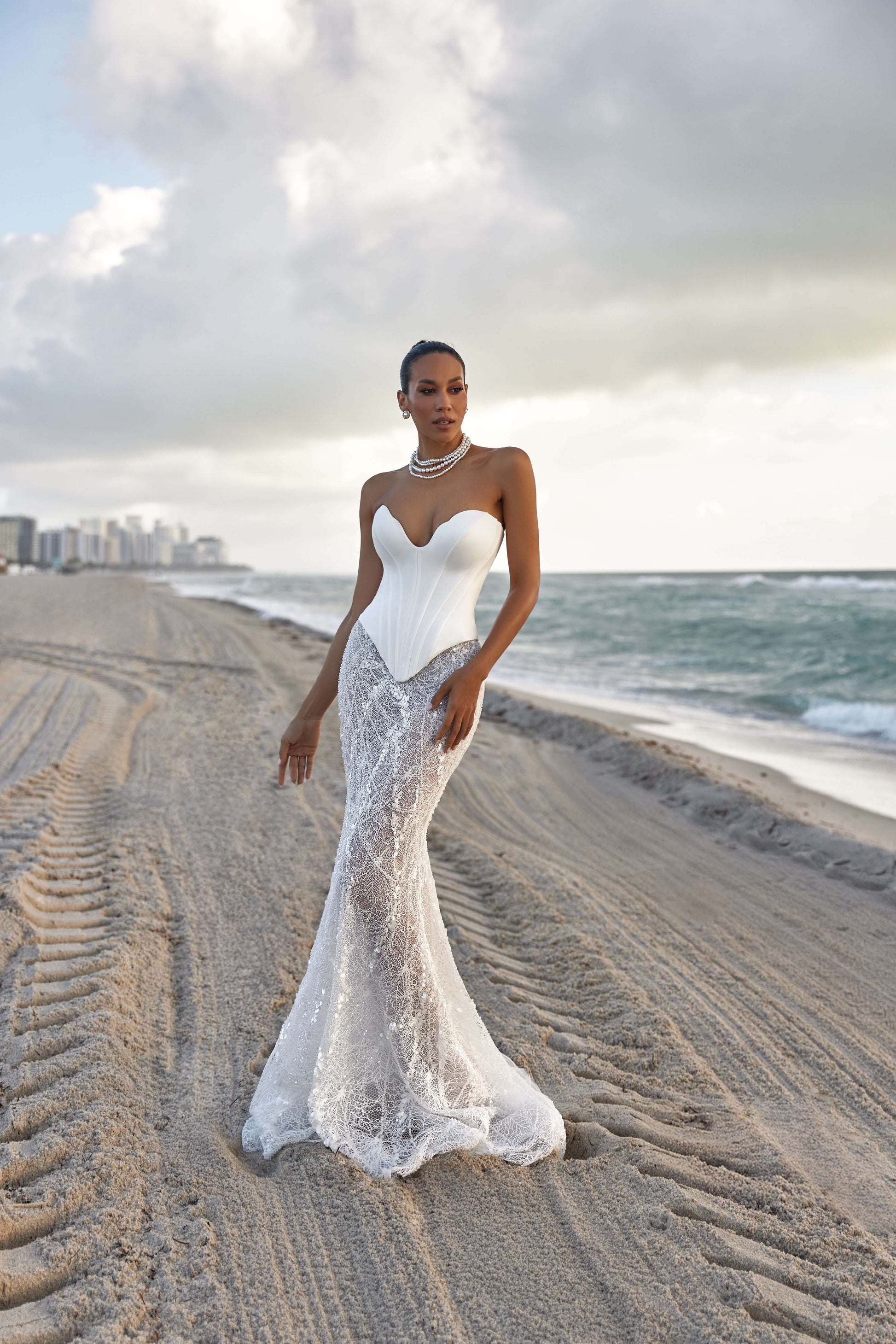 Model wearing a modern corset skirt set on the beach with ocean backdrop, embodying elegant style and sophistication.