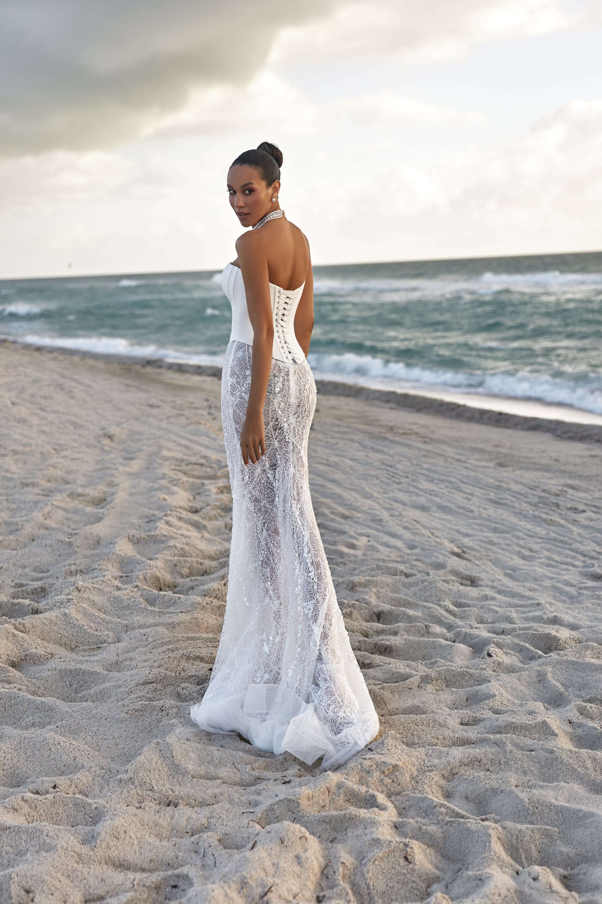 Model wearing a stunning modern corset skirt set on the beach, showcasing the intricate lace design and serene ocean backdrop.