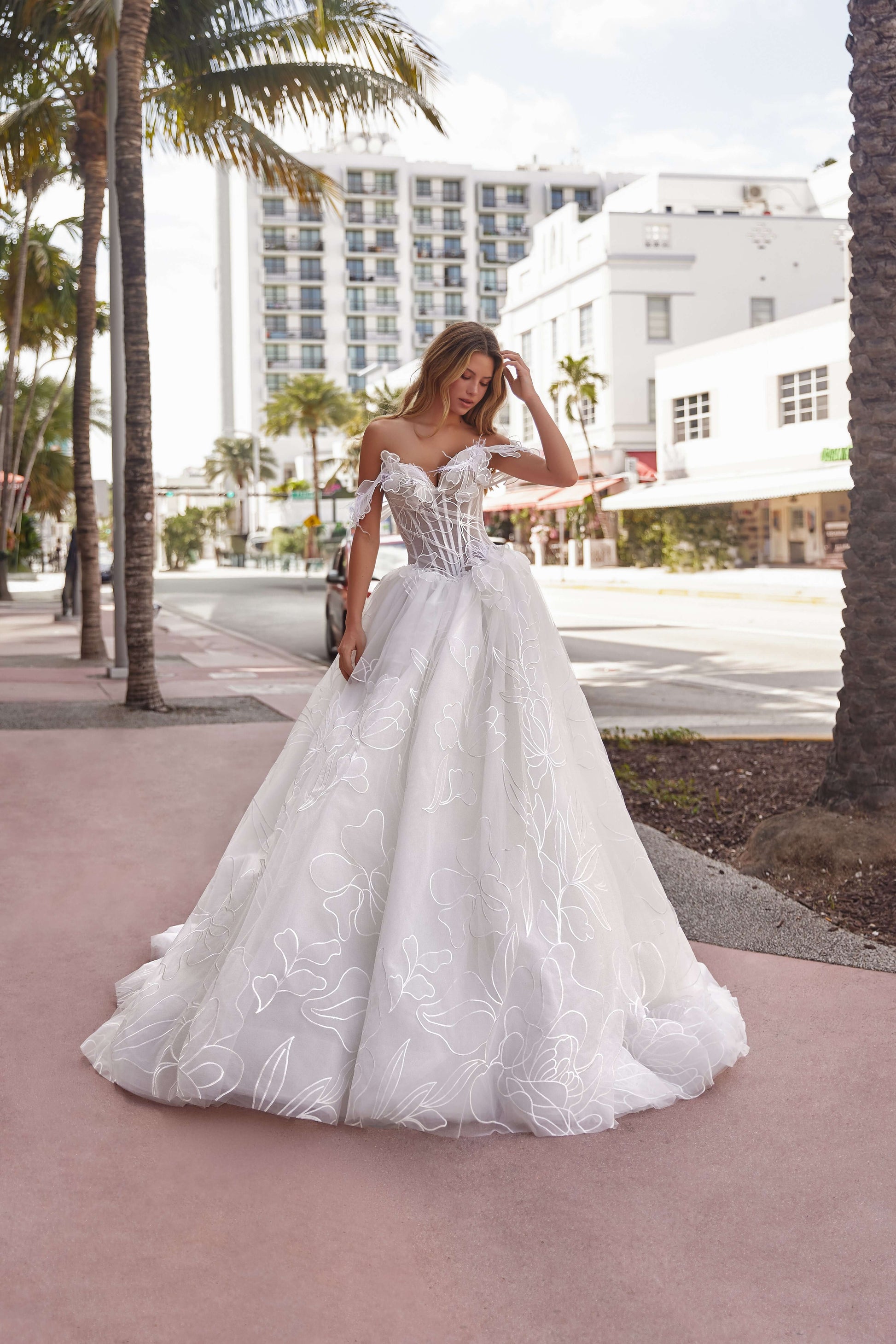 Elegant A-line off-the-shoulder dress with floral details, model posing on a city street surrounded by palm trees.