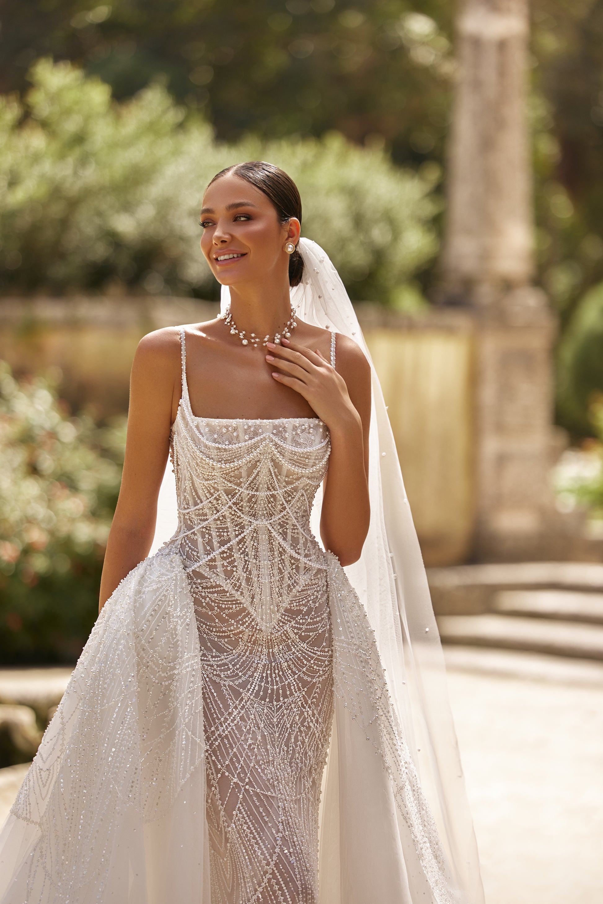 Luxurious wedding dress with lining featuring intricate lace and pearl details, model wearing a stunning bridal look outdoors.