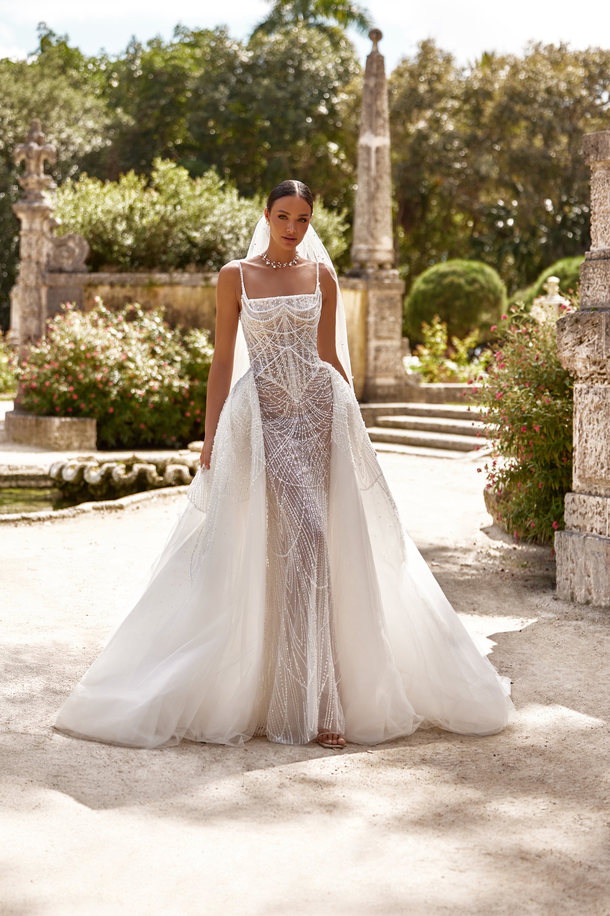 Beautiful model wearing a detachable lace overskirt dress in a lush garden setting with intricate details.