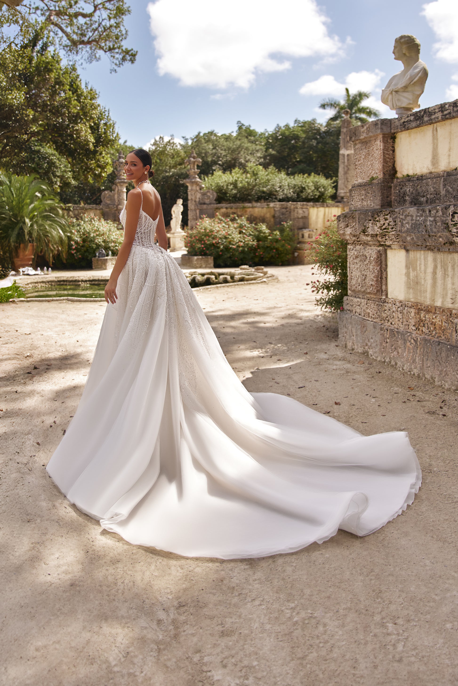 Elegant woman wearing a detachable lace overskirt in a scenic outdoor garden setting.