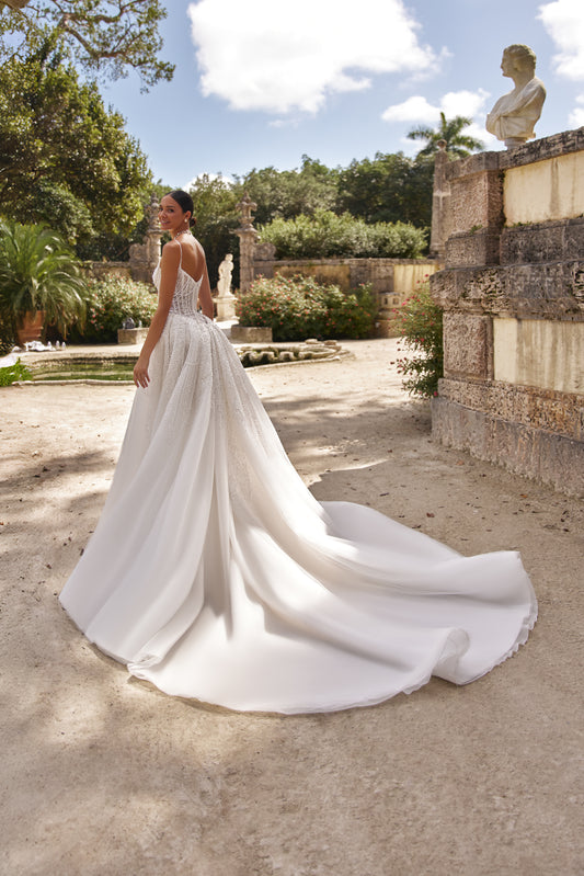 Elegant woman wearing a detachable lace overskirt in a scenic outdoor garden setting.