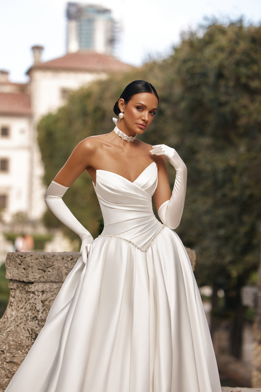 Elegant woman wearing a luxurious ball gown with a flattering corset and long gloves in a scenic outdoor setting.