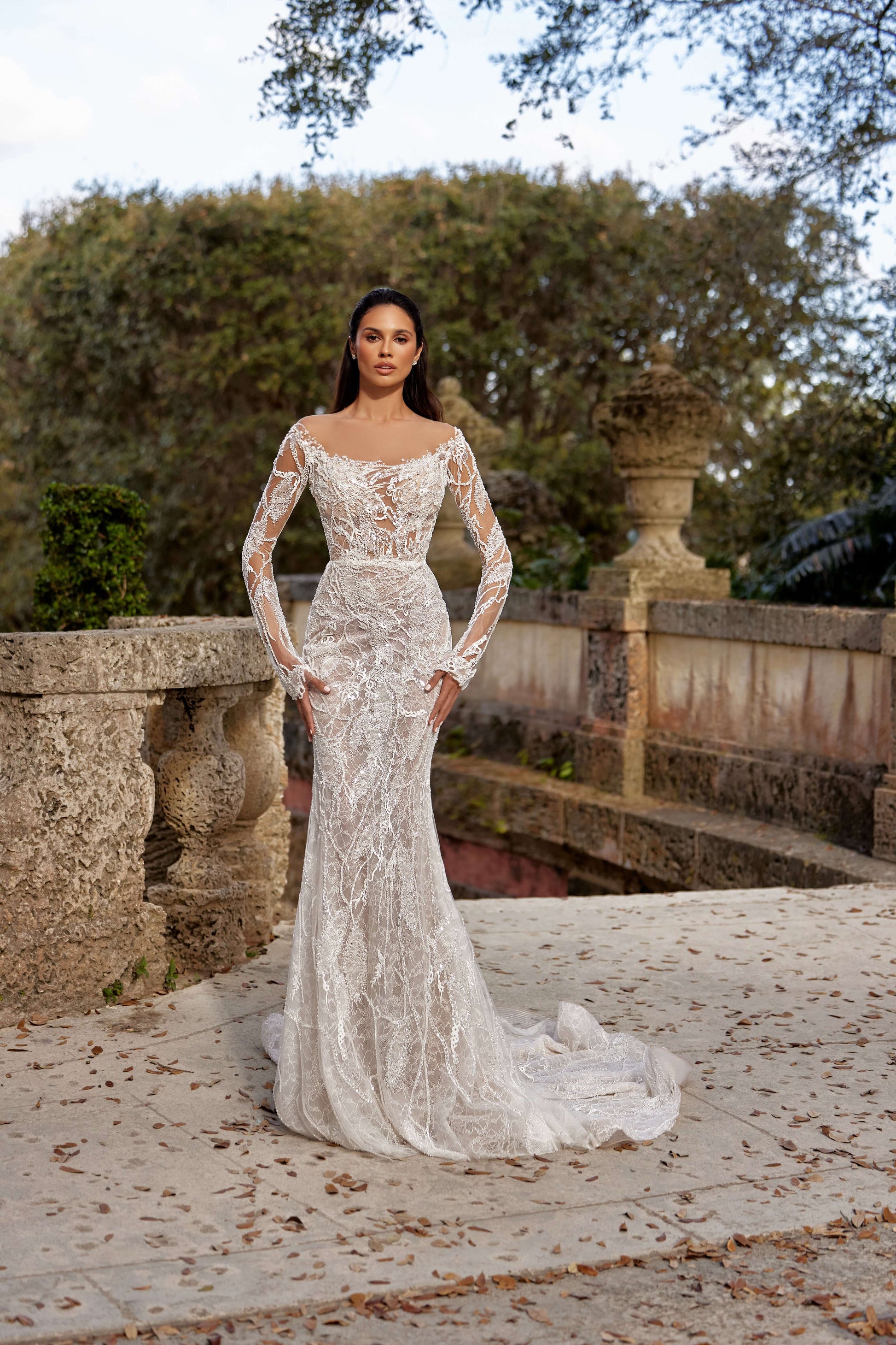 Textured wedding dress with lining showcased on a model in an outdoor setting surrounded by greenery and ornate architecture.