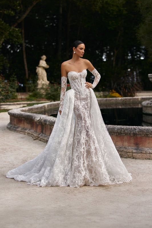 Bella wedding dress with detachable train elegantly displayed outdoors near a serene fountain.