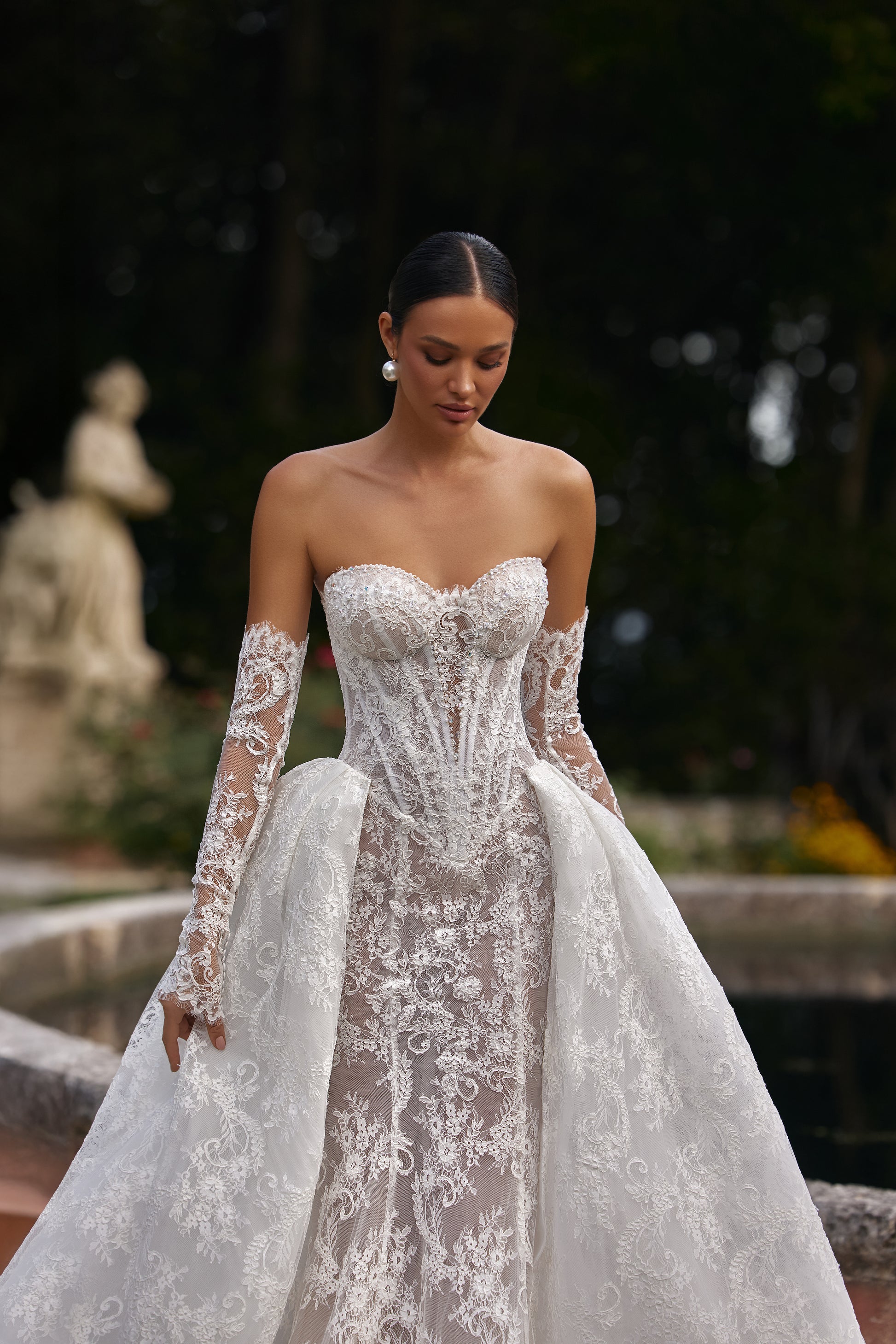 Bella wedding dress with detachable train worn by a model in a garden setting, showcasing intricate lace details.