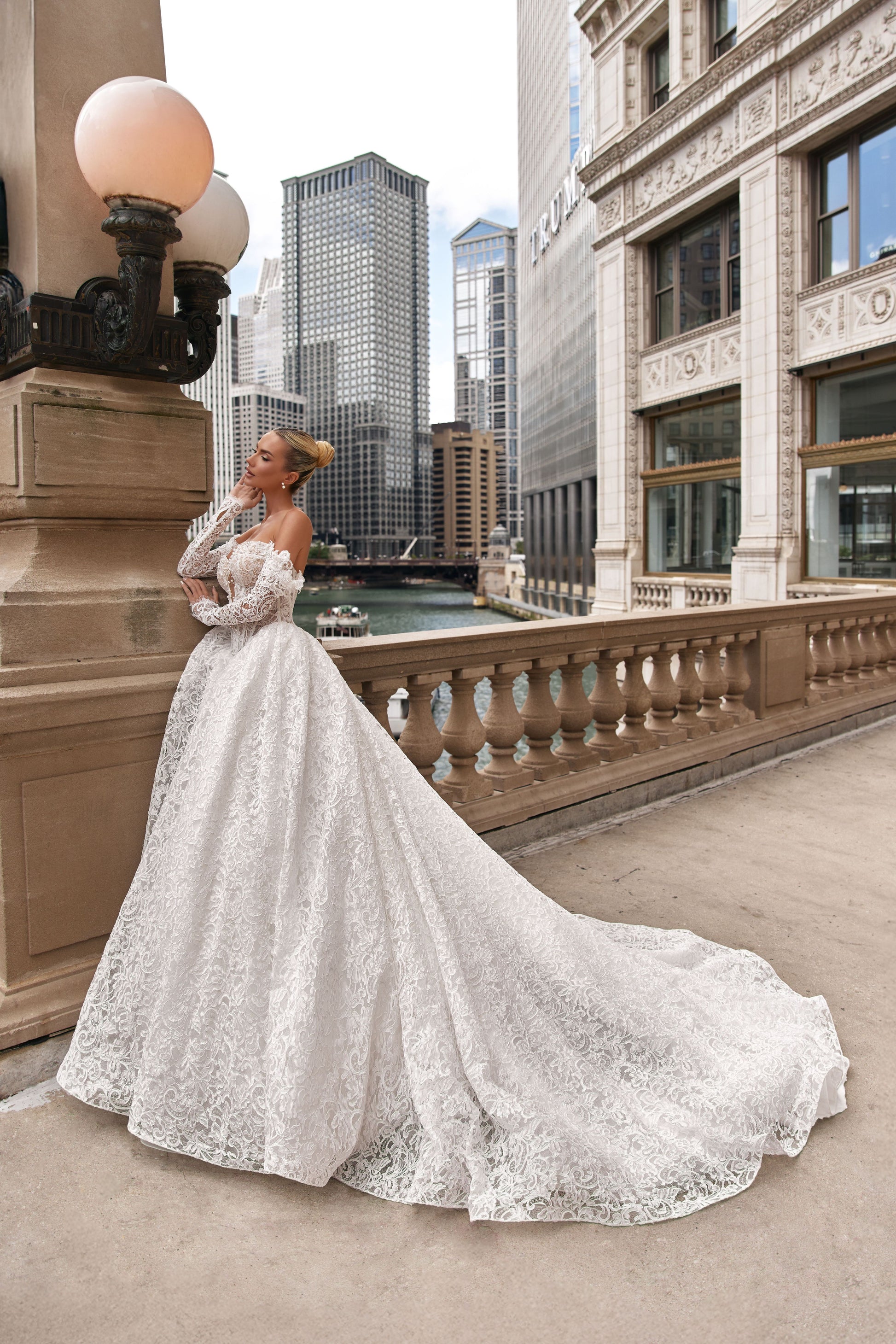 Model wearing a romantic A-line lace dress with voluminous skirt and off-shoulder sleeves in a city setting.