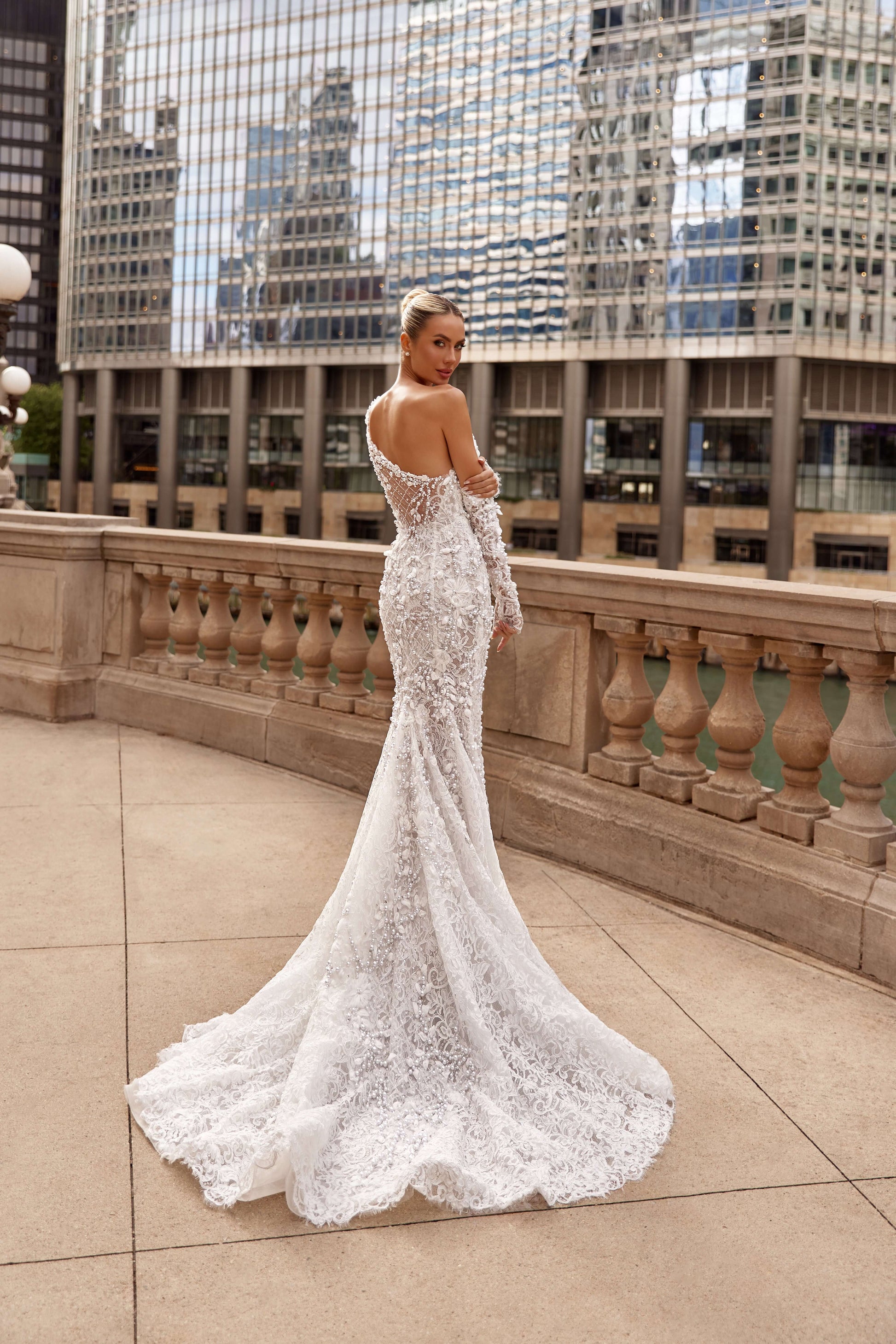 Alegra asymmetrical neckline mermaid dress featuring intricate lace detailing, showcasing a stunning silhouette in a city backdrop.
