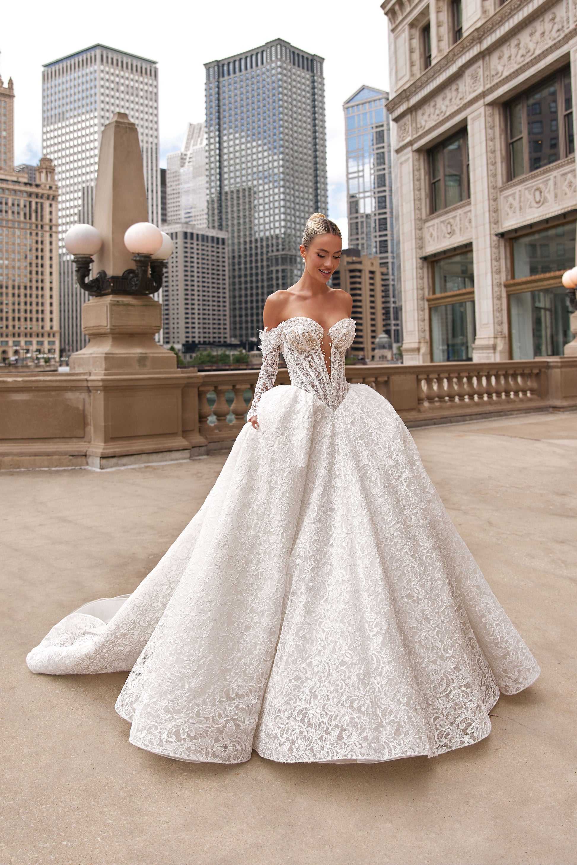 Romantic A-line lace dress with voluminous skirt and off-shoulder sleeves, set against a city skyline.