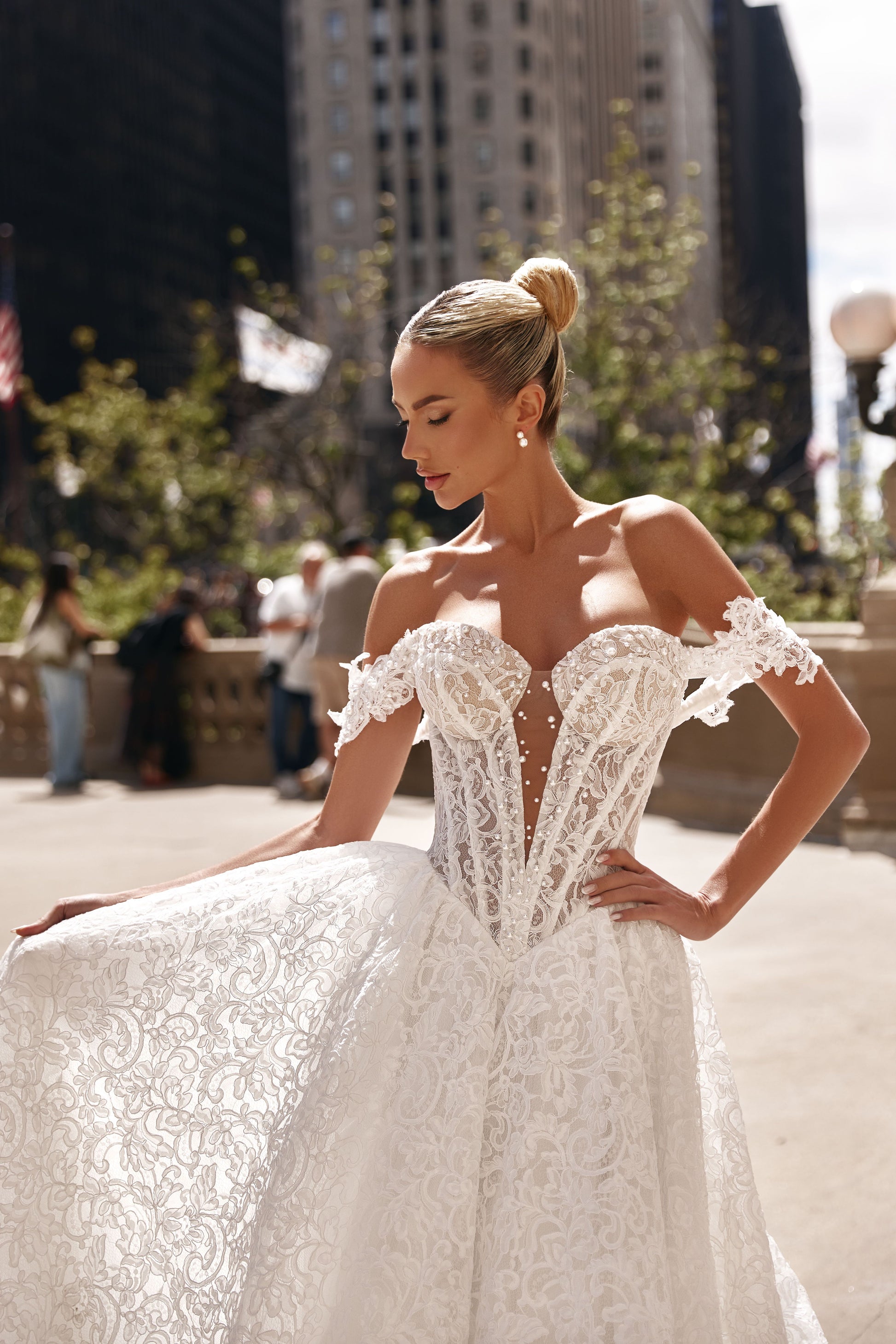 Beautiful model wearing a romantic A-line lace dress with voluminous skirt and off-shoulder sleeves outside in the city.